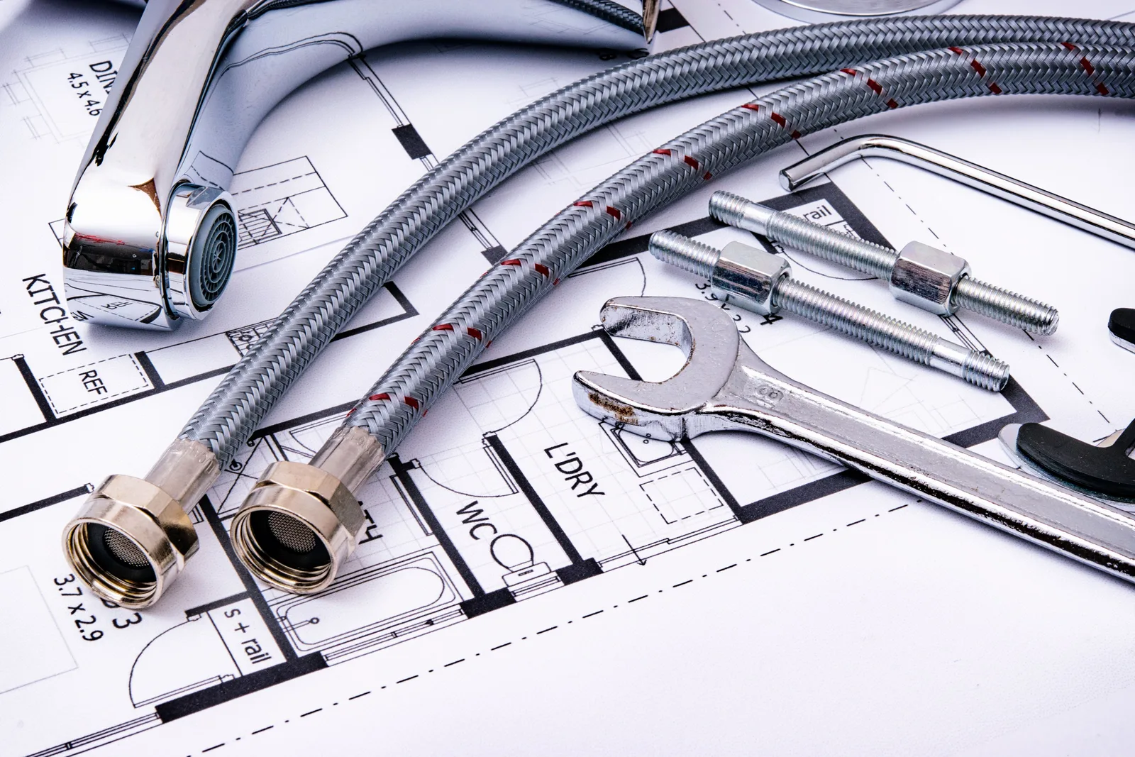 Braided supply hoses, a faucet and an adjustable wrench laid out on a set of floor plans