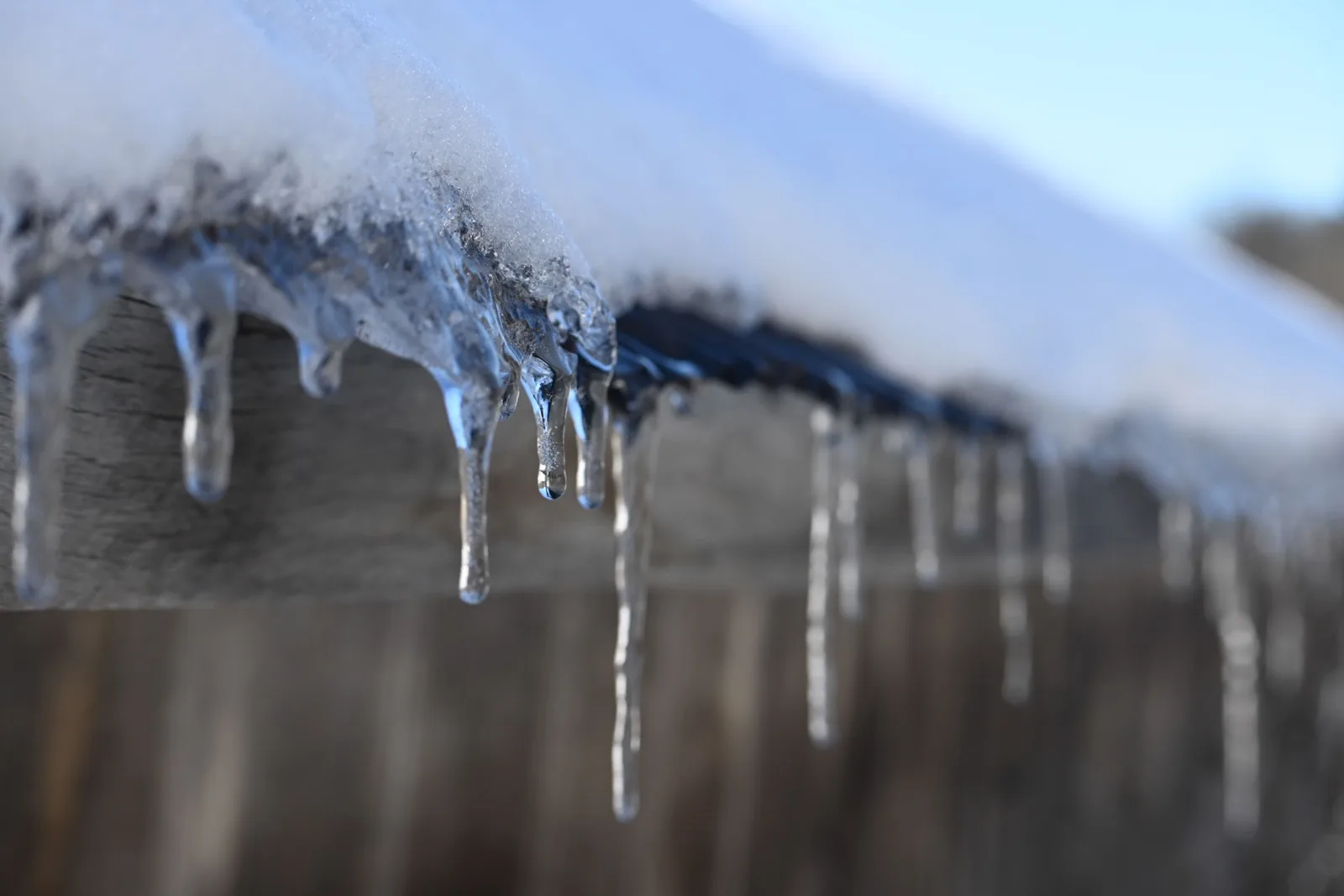 A row of icicles hanging from the snow covered edge of a roof after heavy snowfall.