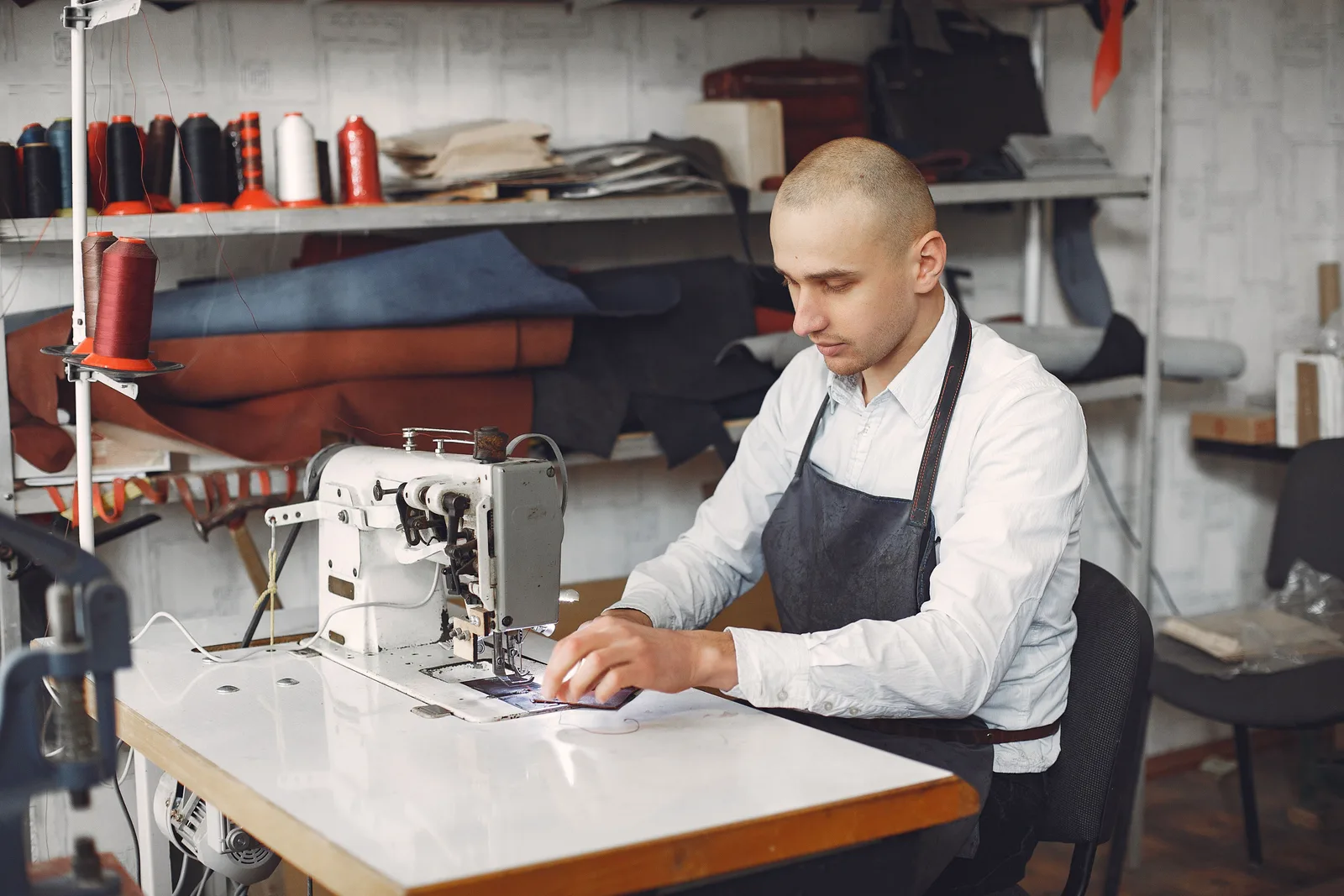 A leatherworker in an apron guides material through an industrial sewing machine.