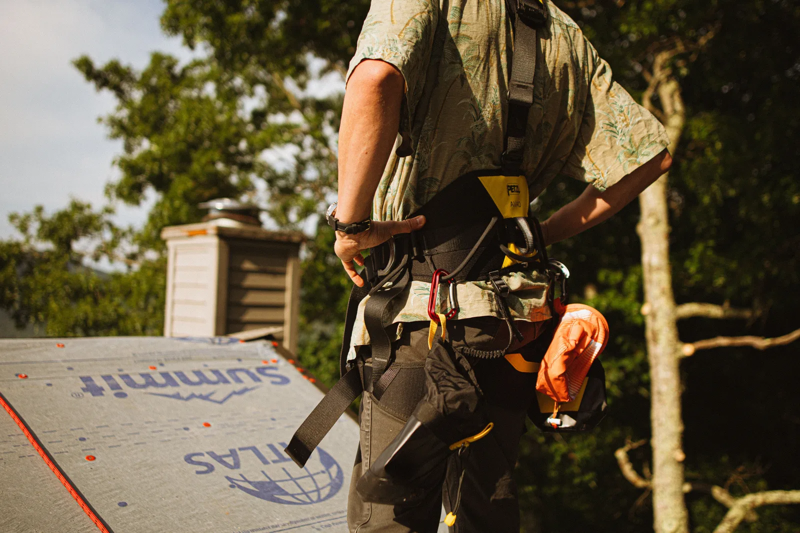 Roofer wearing a full fall arrest harness and tool belt, standing on synthetic underlayment