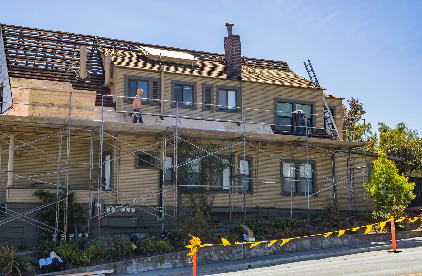 Two storey house wrapped in scaffolding with workers on the roof beside the chimney