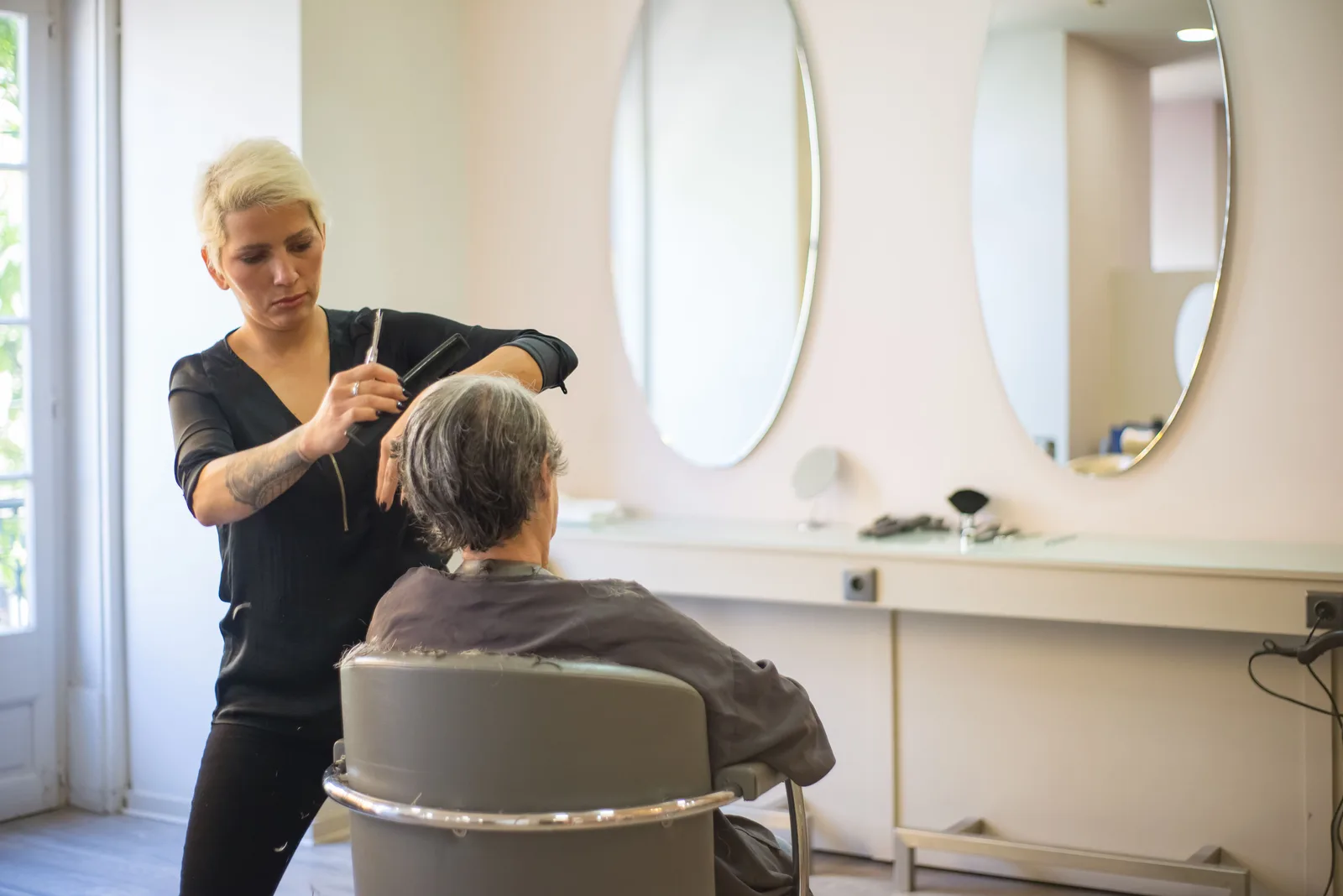 Stylist cutting a seated client’s hair in a bright salon with round mirrors along the wall