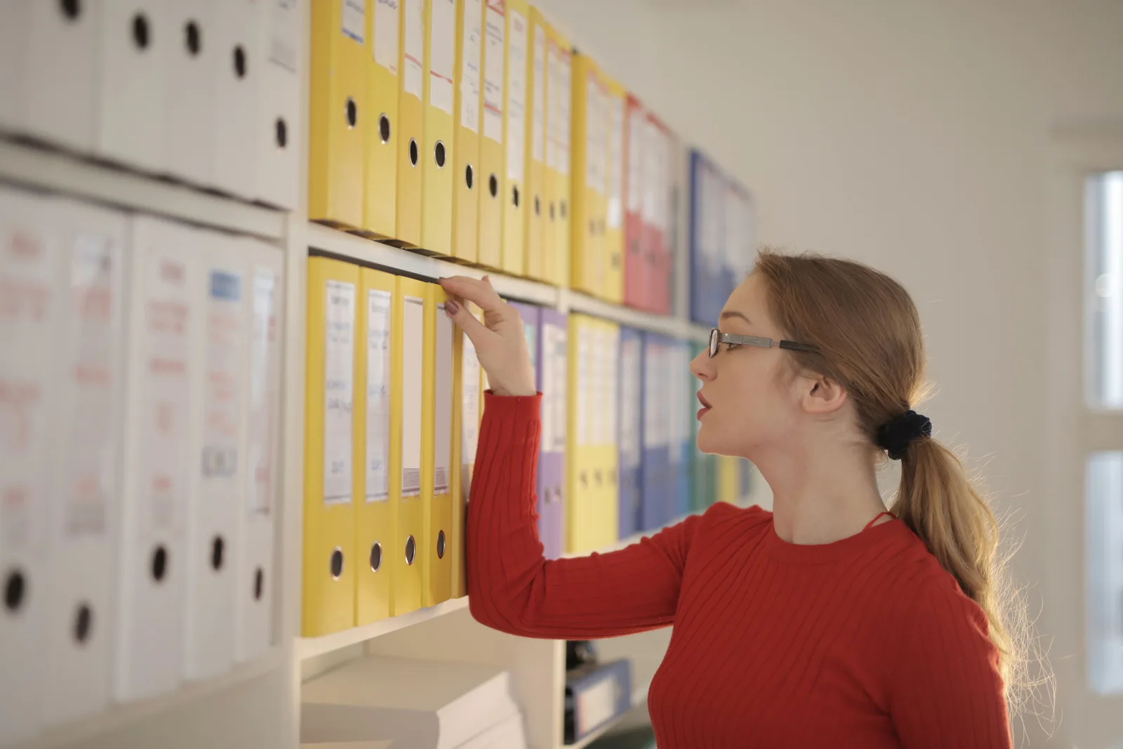 Woman pulling a labelled lever arch file from an office shelf of coloured binders