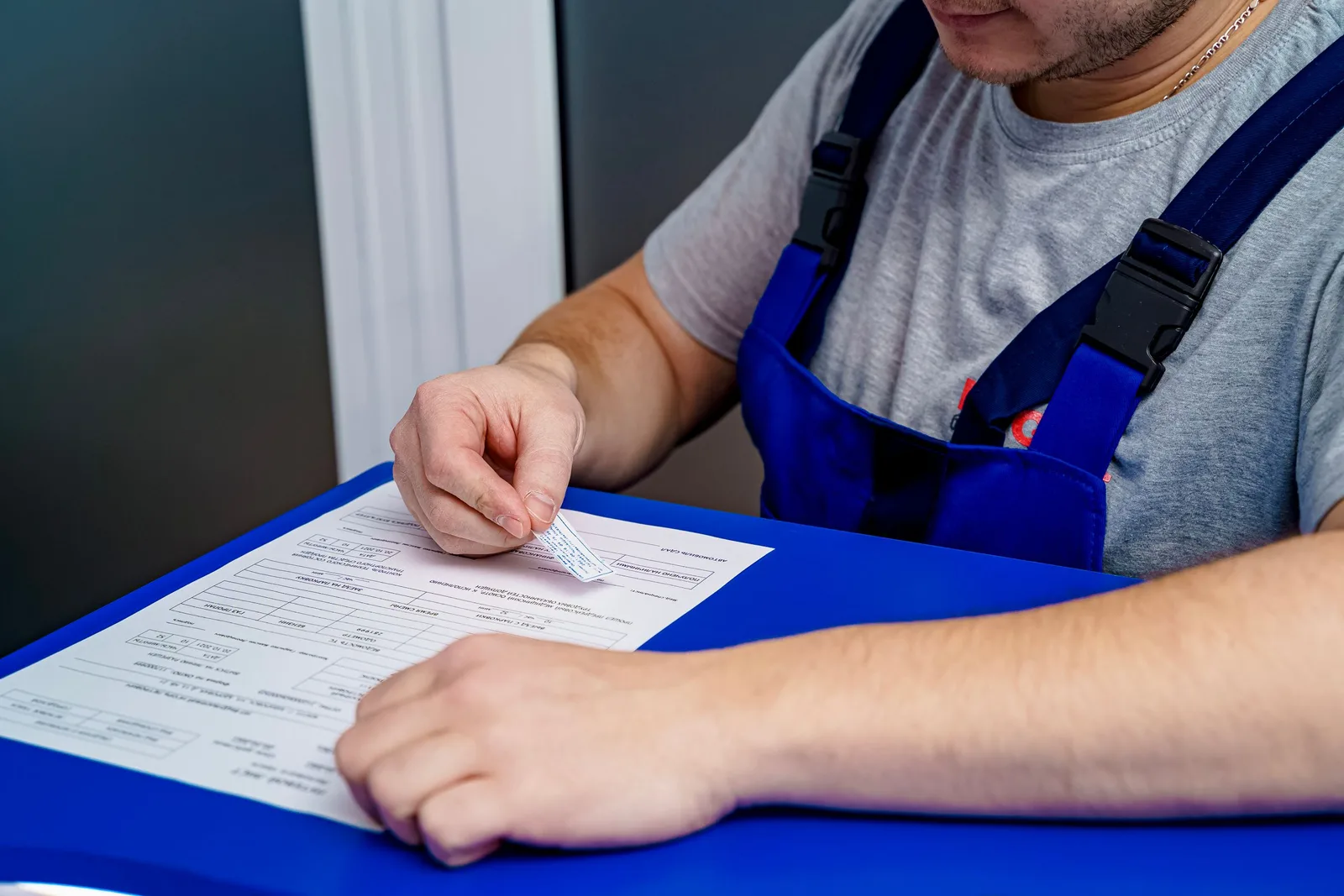 Person in work overalls filling in a printed form at a desk