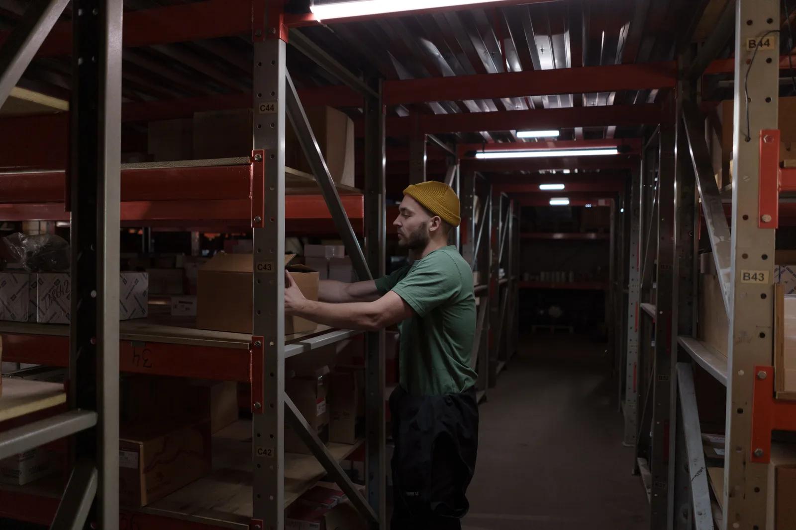 Worker placing a box onto a rack in a narrow warehouse storeroom