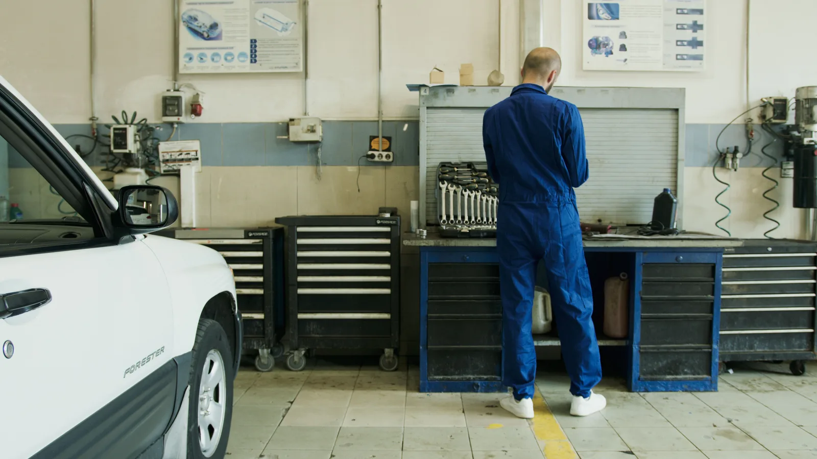 Mechanic in blue overalls working at a tool bench in an independent repair garage with a car alongside