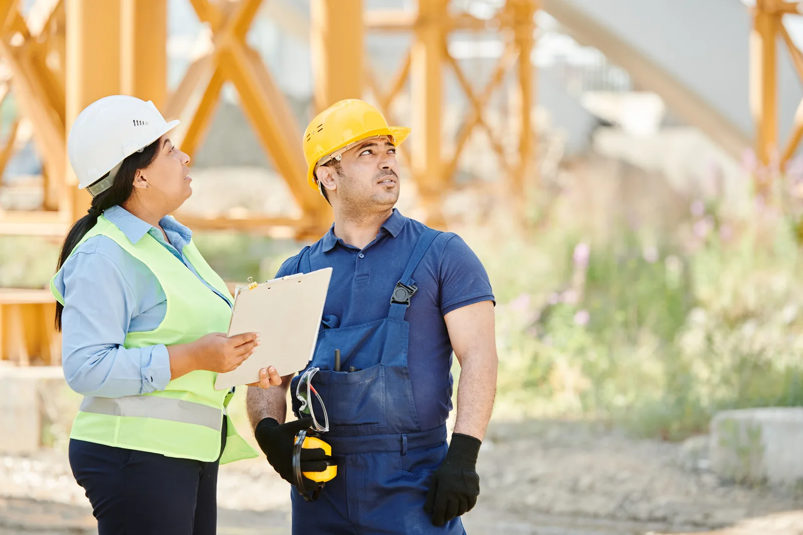 Two workers in hard hats and high visibility safety gear looking over site plans at an outdoor construction site