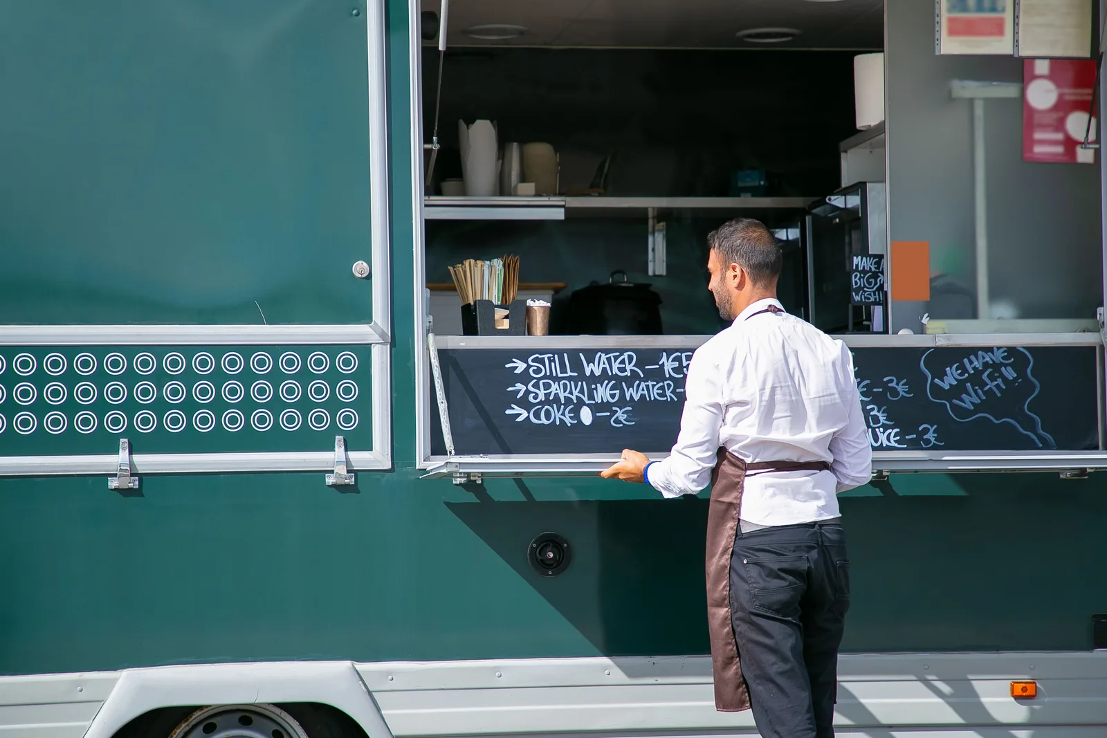 Owner opening the serving hatch of a food truck beside a chalk menu board.