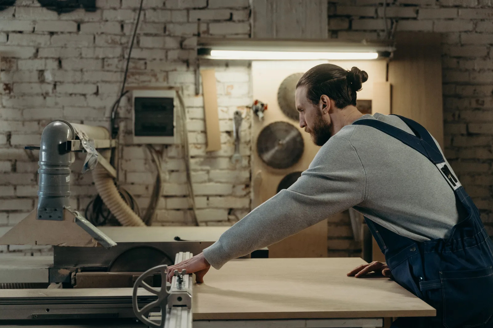 Carpenter feeding a board through a panel saw in a small joinery workshop.