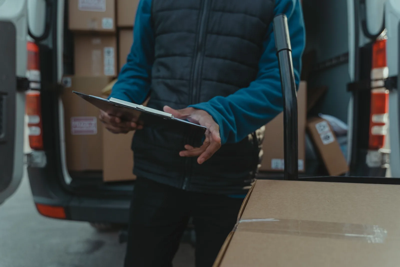 Courier checking a clipboard beside a van loaded with parcels