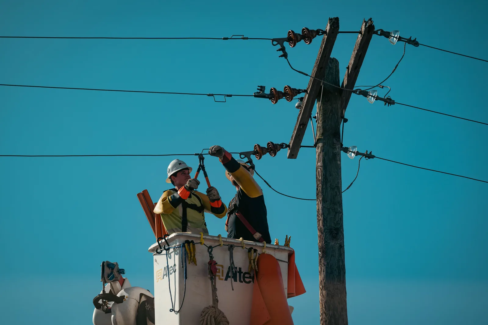 Two electricians in lift buckets working on the crossarm of a utility pole