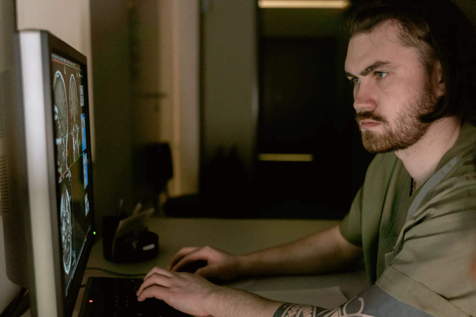 A clinician studying scan images on a monitor at a darkened reporting workstation
