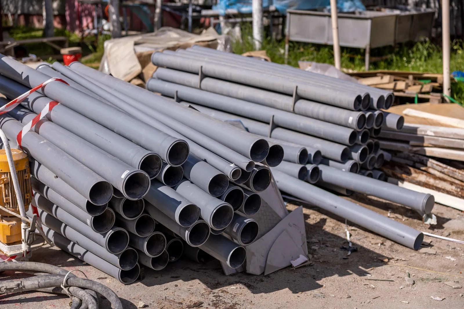 A stack of gray PVC pipe lengths on the ground at a contractor's yard