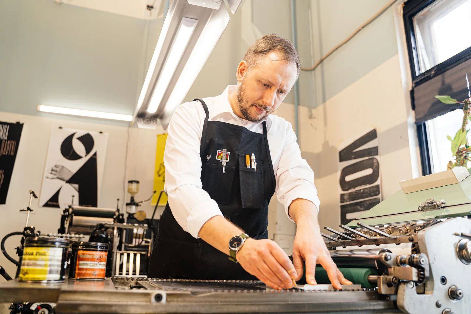 A printer in a work apron feeding sheets into a small press in a print studio
