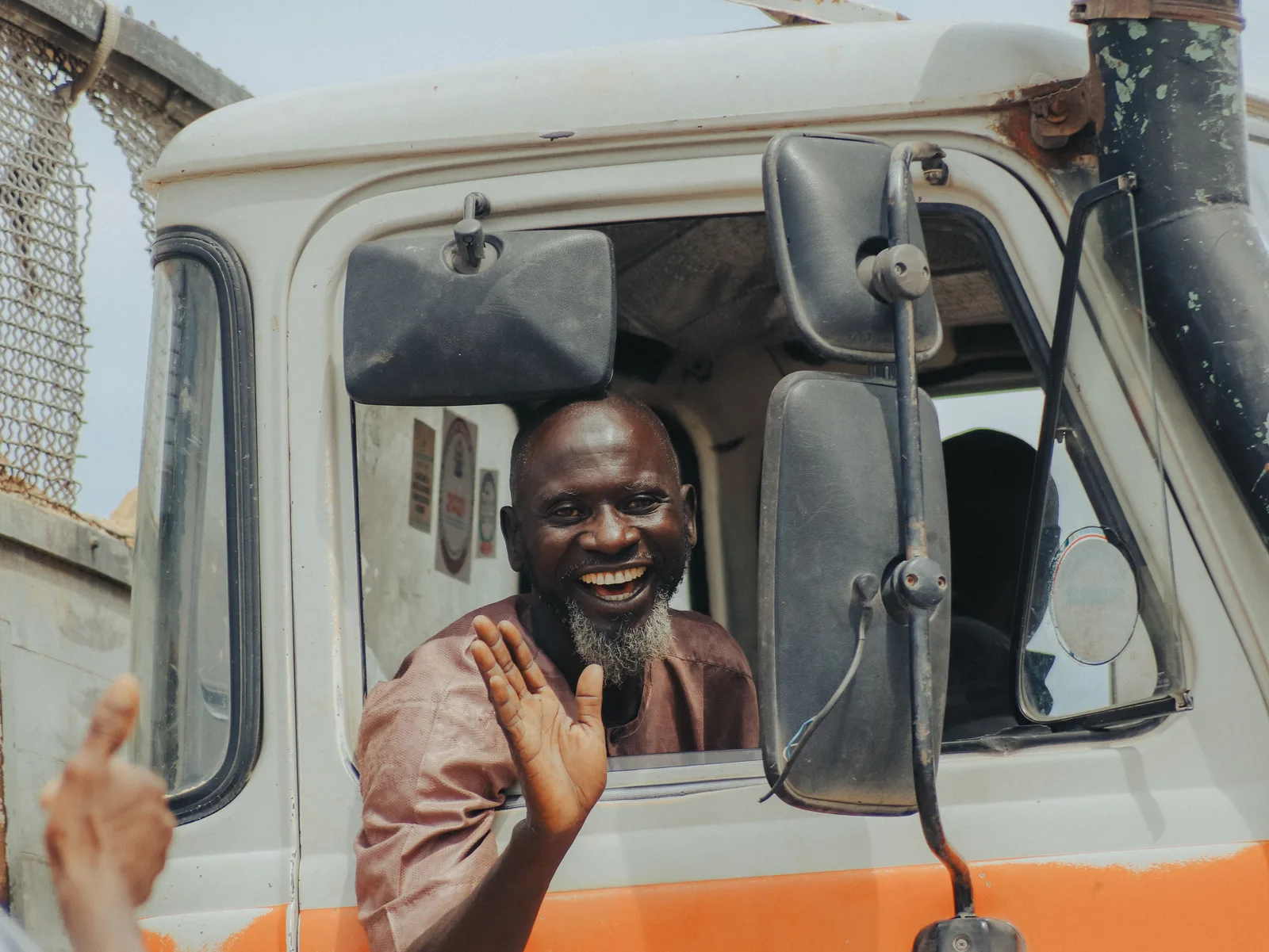 A truck driver leaning out of the cab window of his rig and waving