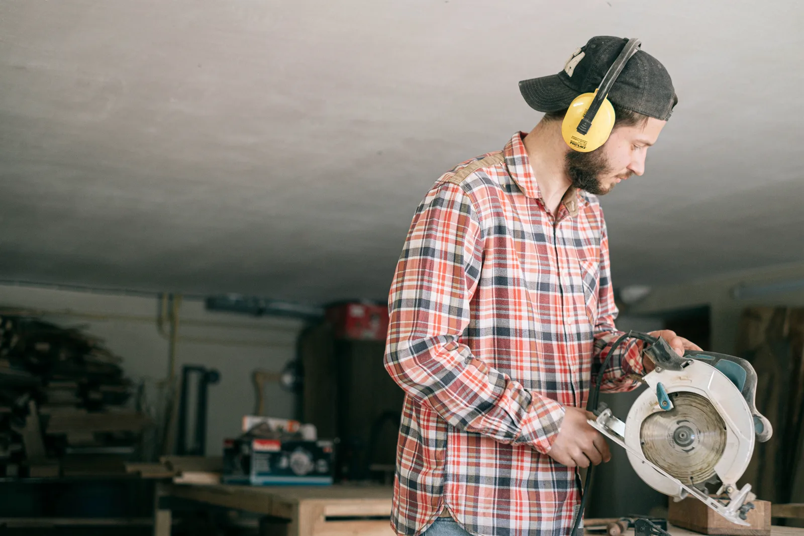 A tradesman in safety glasses cutting a board with a circular saw in his workshop.