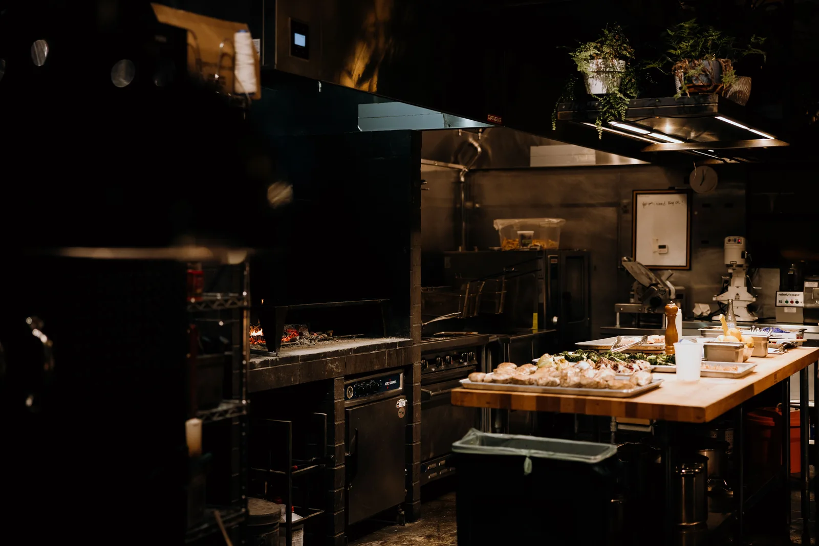 Restaurant kitchen with an open grill and a wooden pass counter laid out with trays of prepared food before service