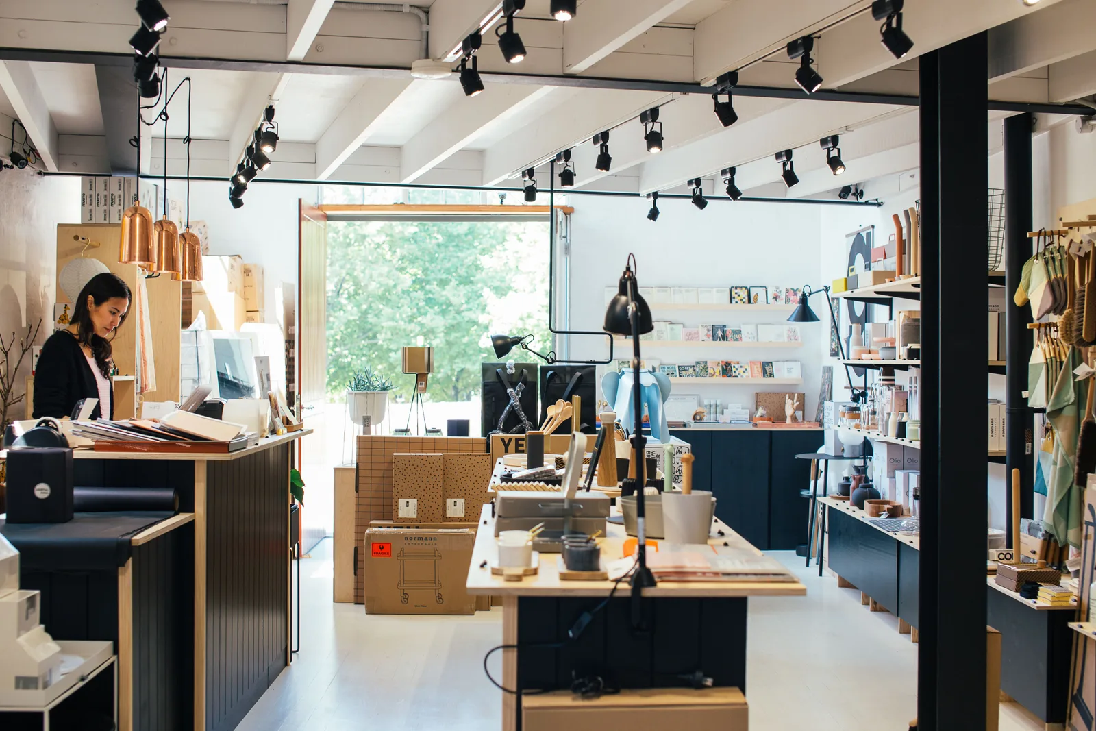 A shop owner works at the checkout counter of a small design and homeware store surrounded by stock