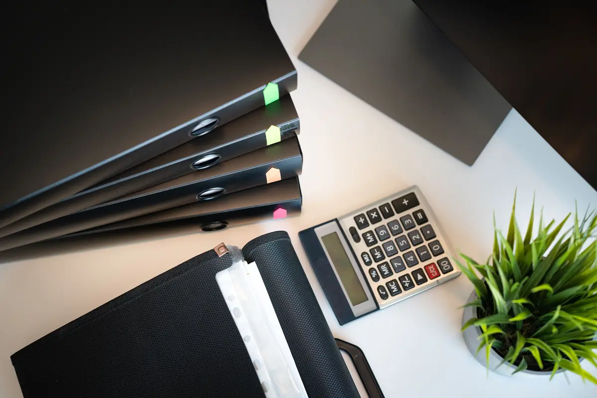 Top view of a tidy office desk with filed paperwork, a calculator and a small plant.