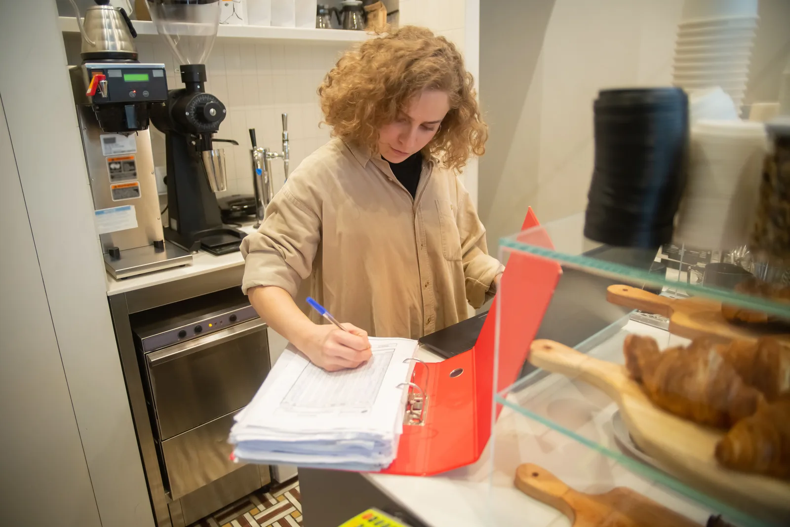 Cafe owner writing in a ring binder of paperwork beside her espresso grinder