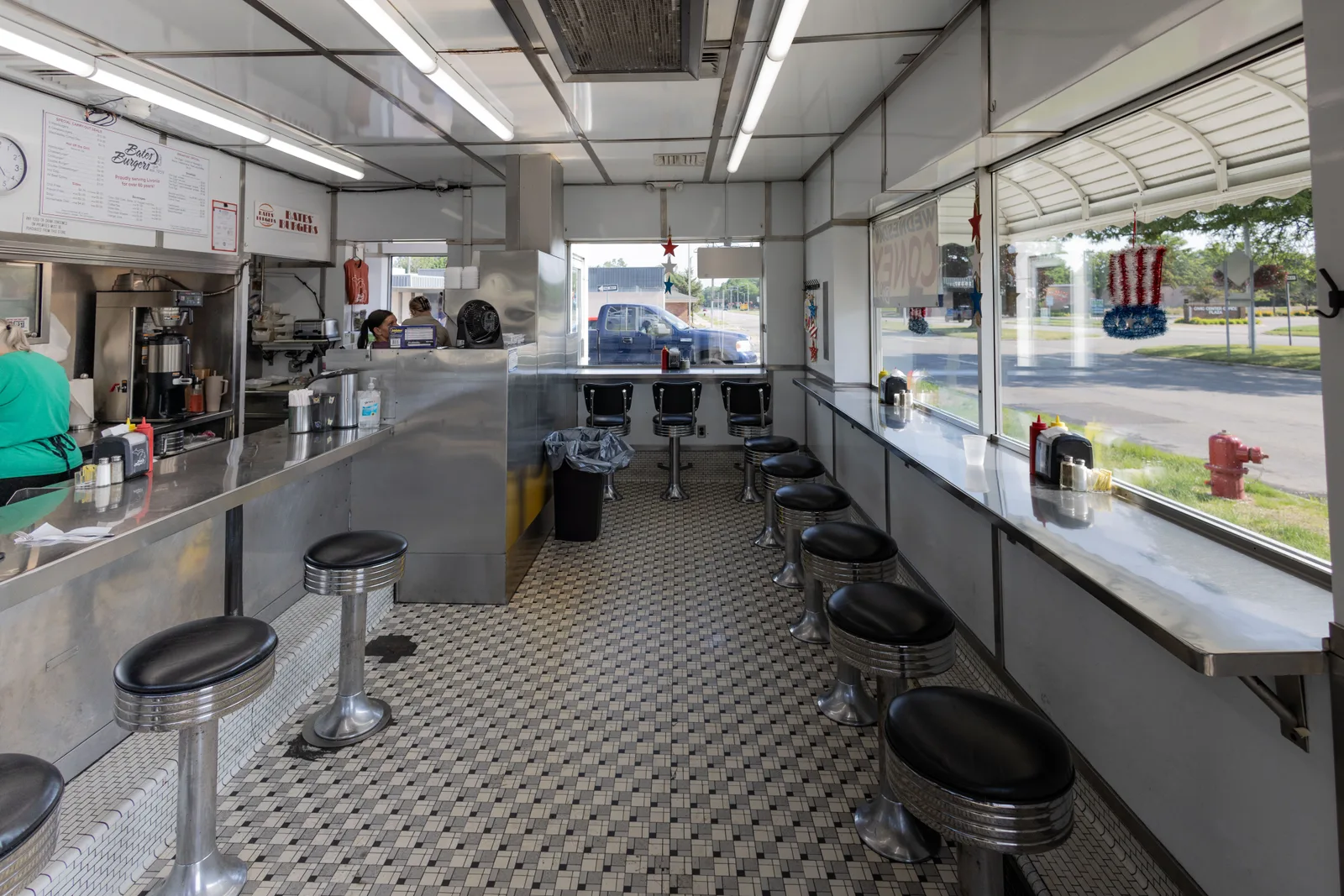 The interior of a classic American diner with counter stools, a tiled floor and street windows.