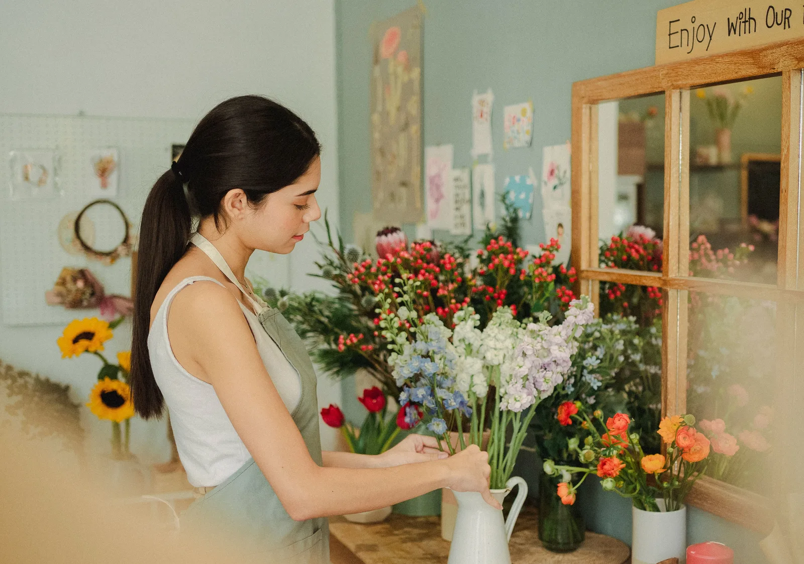 Florist arranging cut stems into a jug at her shop workbench.